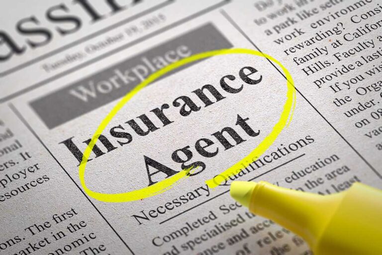 A person reviews a household insurance bill with charts and paperwork spread out on a kitchen table.